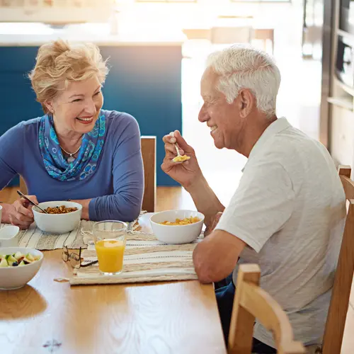 Old couple, smile and eating at dining table with breakfast, healthy food or talk for bonding together. Married, elderly people and happy in home with morning meal, nutrition and love for retirement