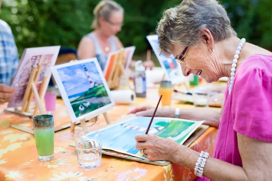 Senior woman is participating an outdoor art class / Une femme âgée participe à un cours d'art en plein air