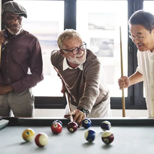 Three senior men are enjoying playing pool together / Trois seniors s'amusent à jouer au billard ensemble
